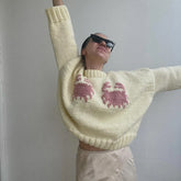 Person wearing a light yellow sweater with pink cat patterns against a plain background